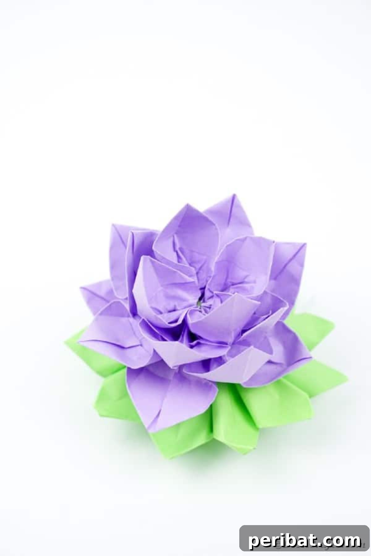 A delicate purple paper lotus positioned on a clean white surface, showcasing its gentle curves.