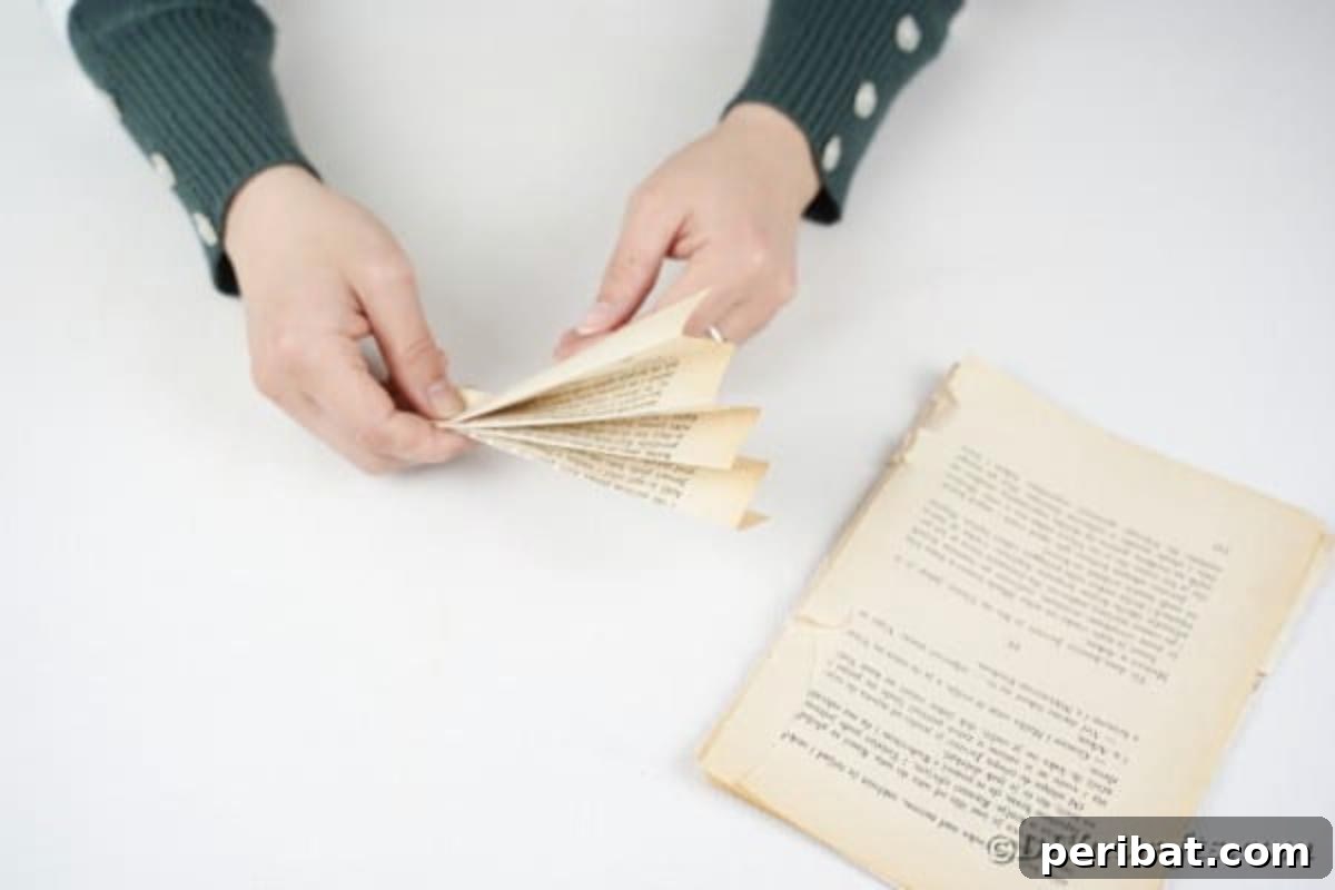 A crafter meticulously folding a book page into an accordion fan shape, a key step for the paper flower