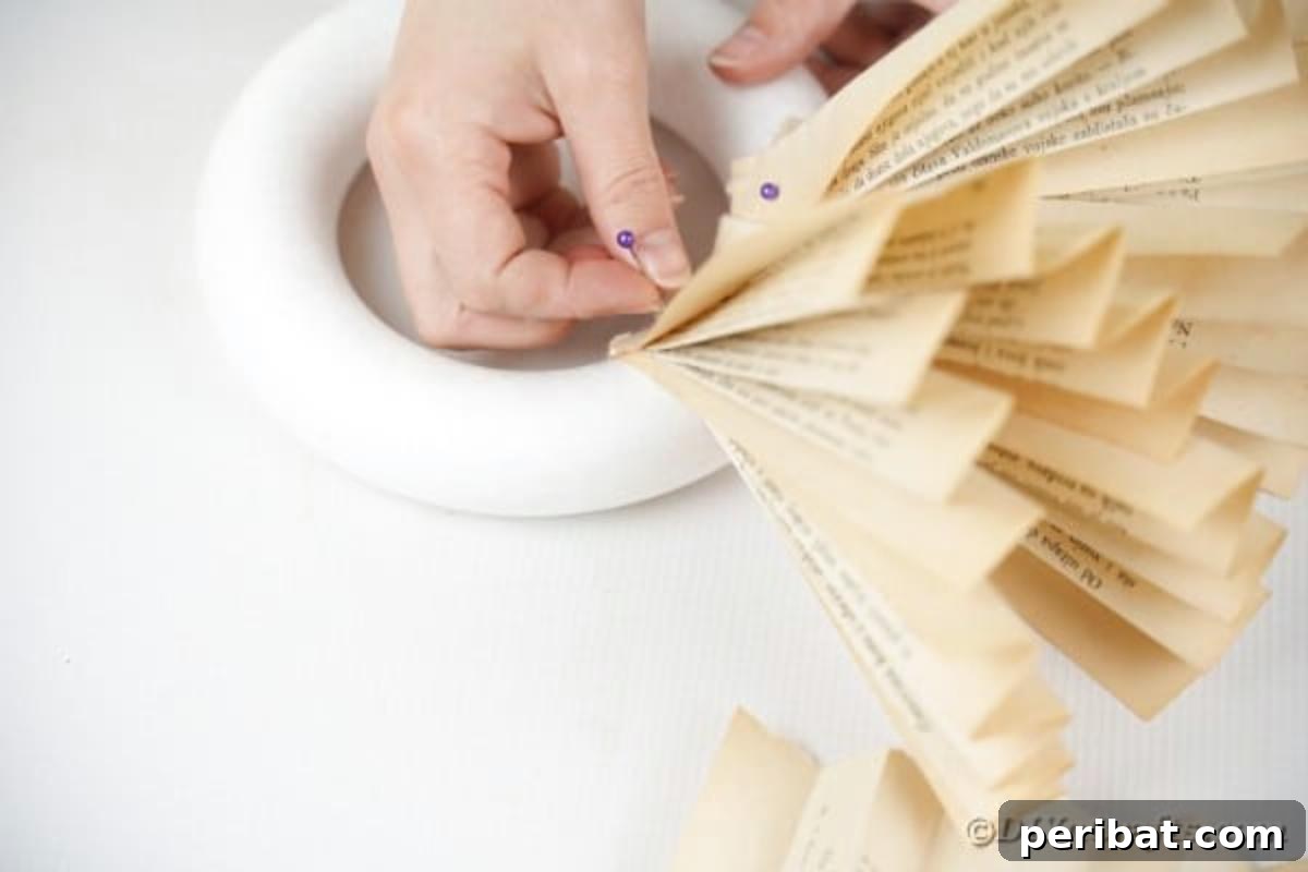 An ongoing assembly of paper fans being pinned to a wreath form, forming the initial layer of the flower