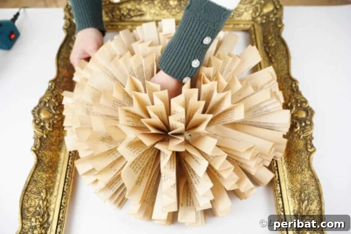 A book page paper flower wreath being carefully placed and secured with hot glue onto the twine-wrapped ornate frame